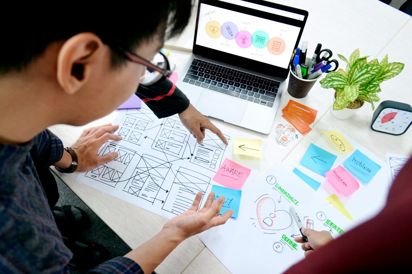Två män samarbetar kring ett UX/UI-designprojekt med trådskisser och post-it-lappar.